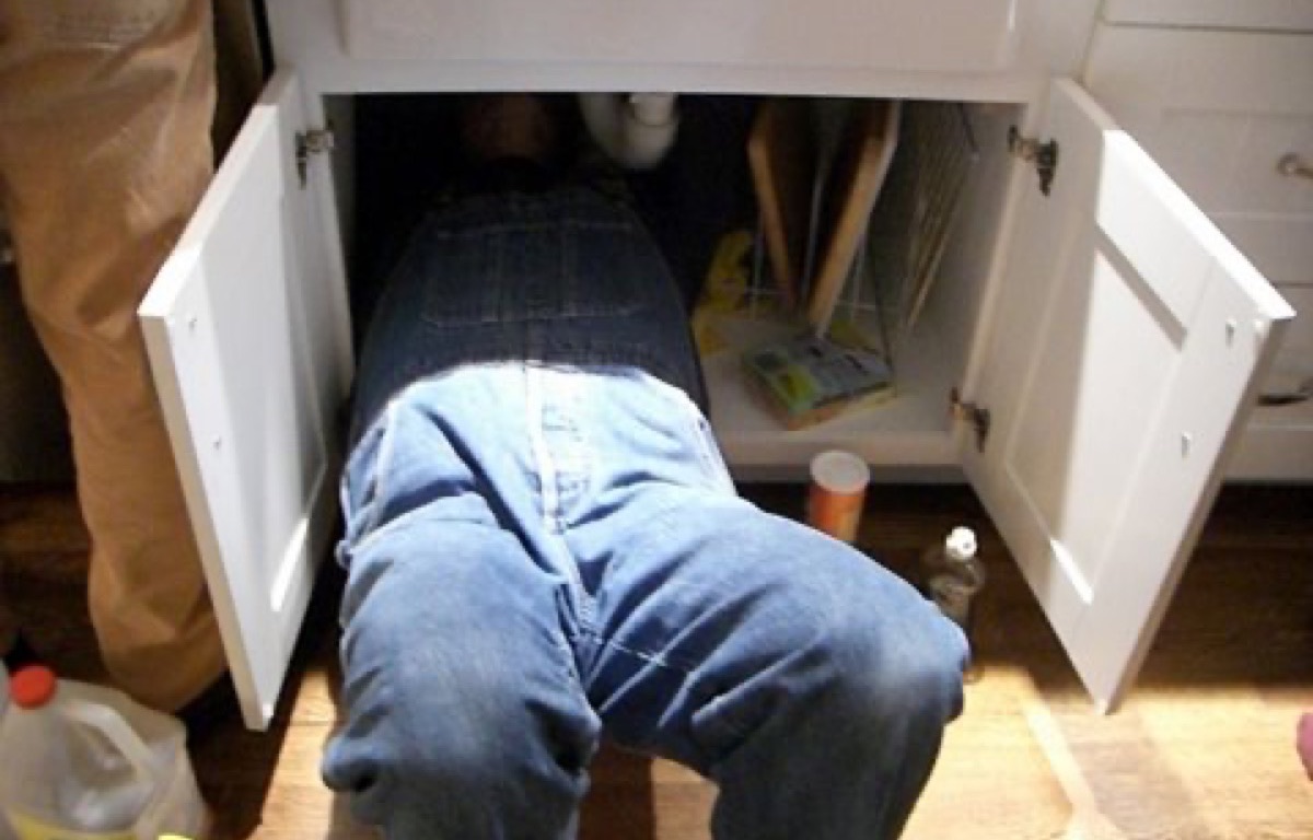 Plumber inspecting pipework inside an under-sink cabinet