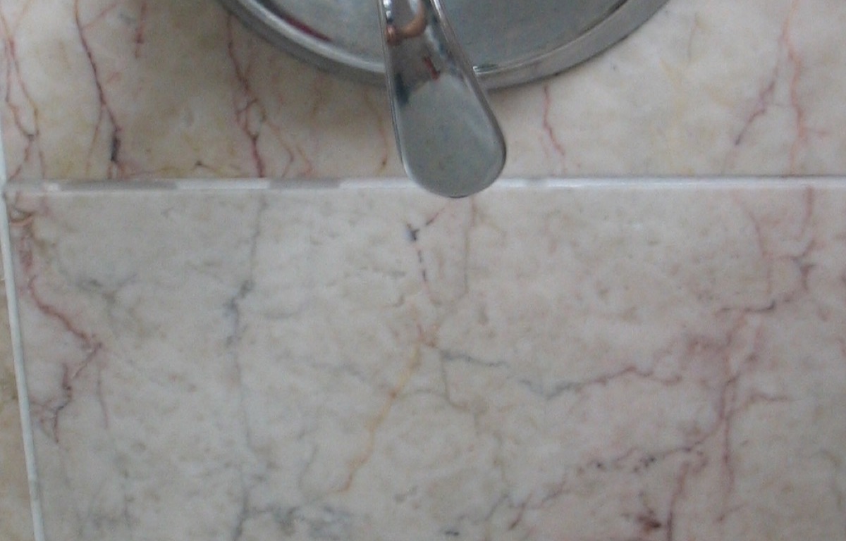 Chrome shower control handle mounted above a bathtub faucet